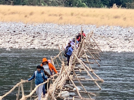 Red bamboo bridge leading to a thatched gazebo over a calm pond in a tea garden in Assam