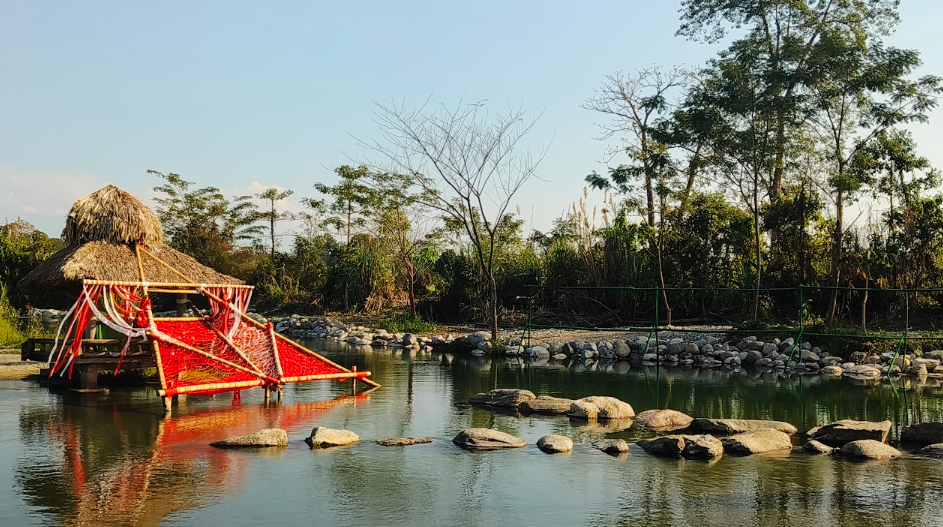 Bamboo hut with a red hammock net built over a calm river pool near Miao