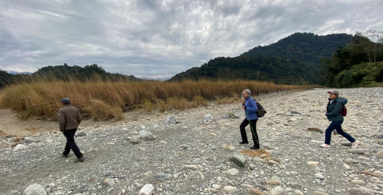 Family walking across a rocky riverbed with East Himalayan foothills in the background near Namdapha