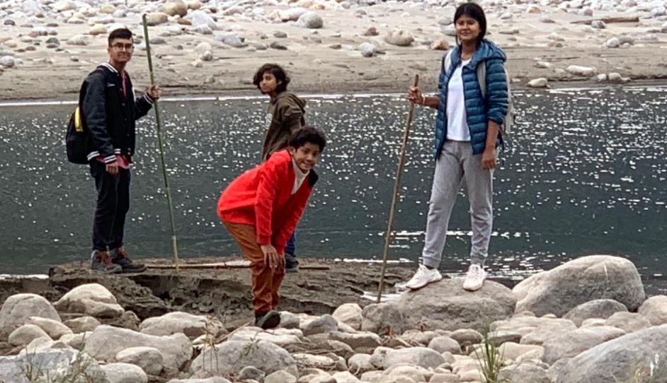 Father and two children playing with sticks on a riverbank during a family trip through Assam and Arunachal Pradesh