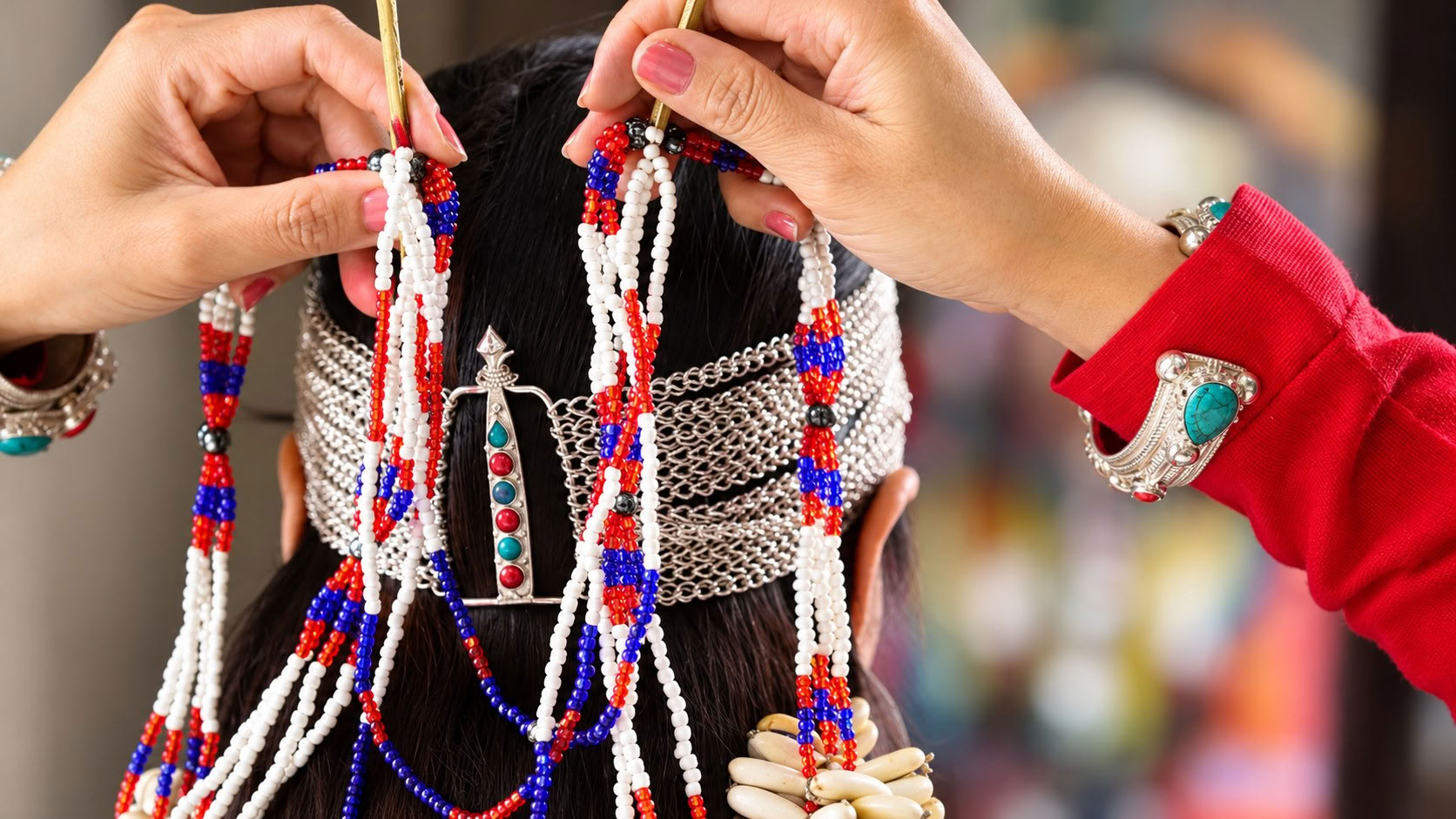 Hands arranging long strings of white, red and blue beads on a woman wearing a silver headband