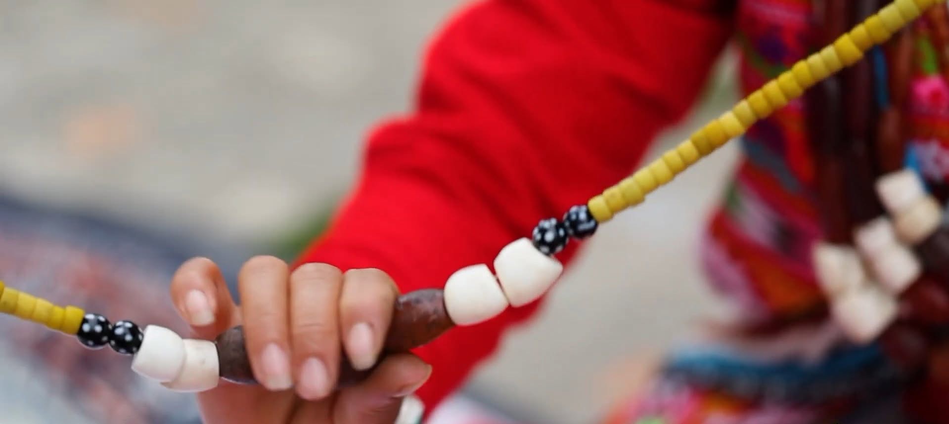 Hands holding a strand of yellow, white and black beads against a red garment