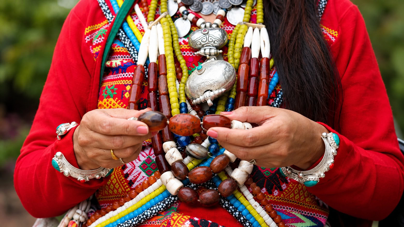 A woman in a red garment holding a heavy necklace of yellow stones, silver and beads