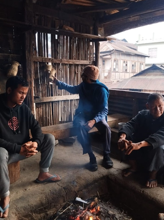 Villagers and visitors sitting around a hearth inside a traditional wooden house