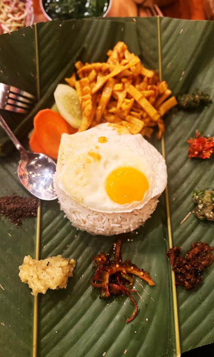Rice with a fried egg, fries and sides served on a banana leaf