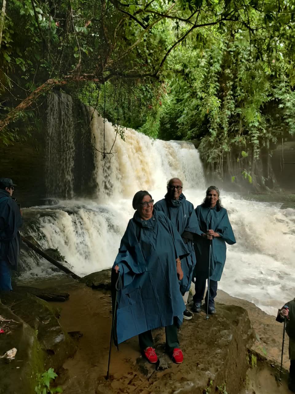 Travellers in blue rain ponchos standing beside a waterfall near Thenzawl