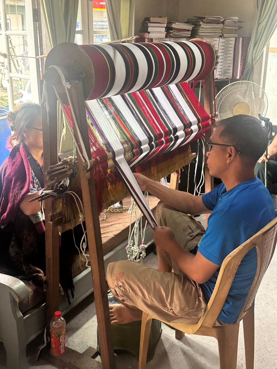 Weaver working at a backstrap loom with striped cloth in Thenzawl