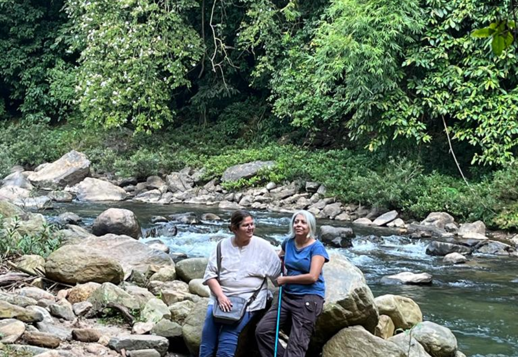 Two travellers resting on boulders beside a forest stream in the Garo Hills