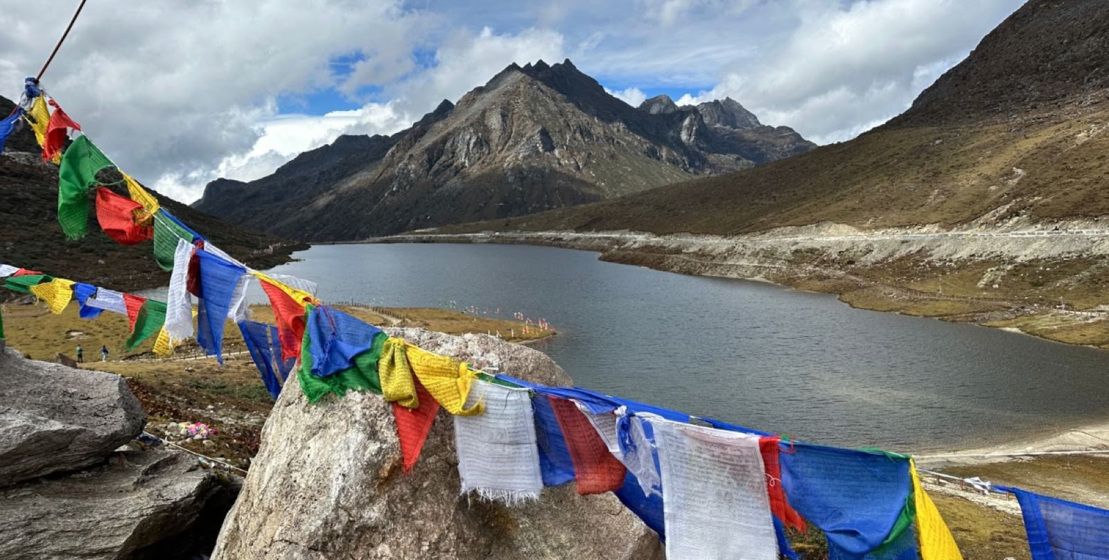 Strings of prayer flags above a mountain lake with rocky peaks in the distance in Arunachal Pradesh