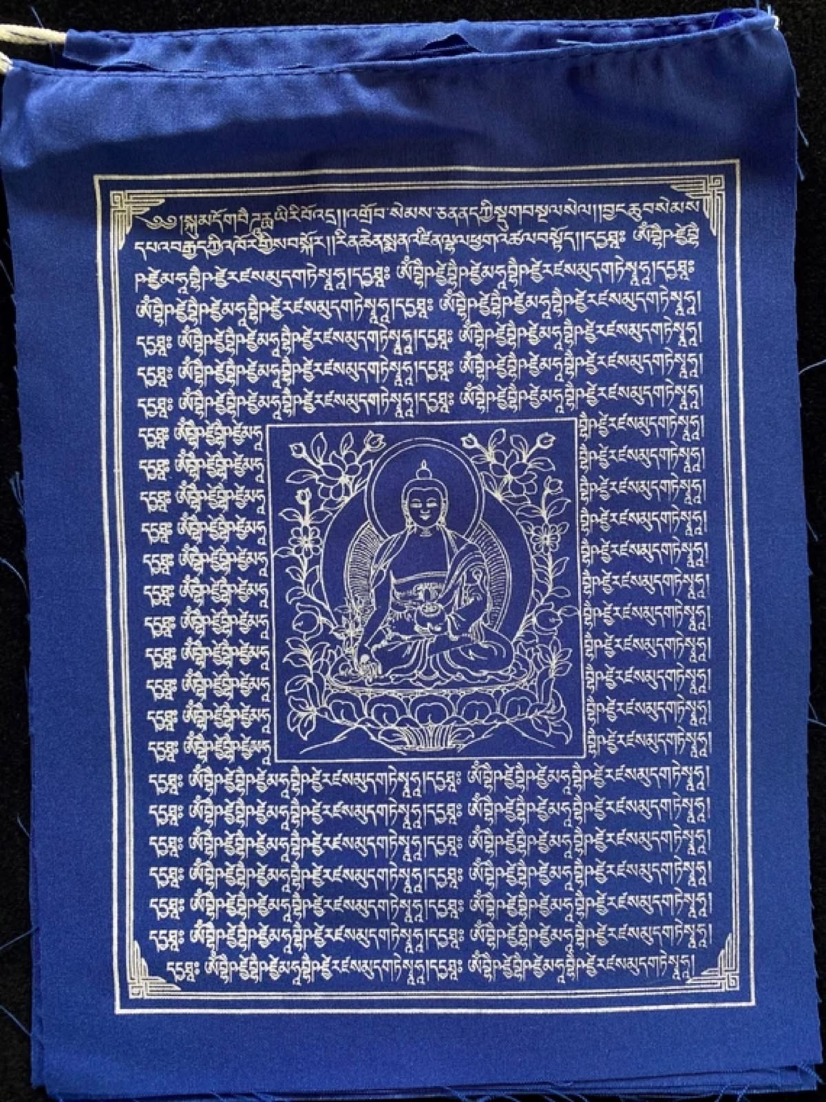 A blue prayer flag printed with a seated Buddha, mantras and an ornamental border