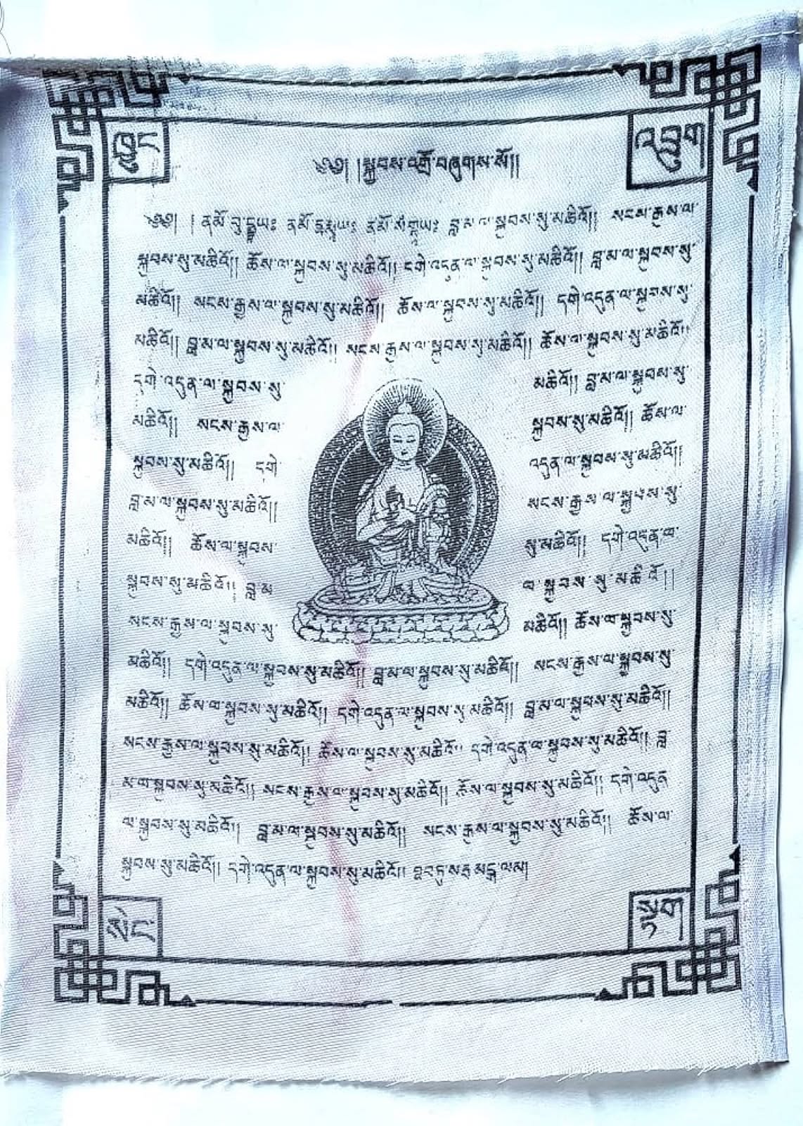 A white prayer flag printed with a seated Buddha and lines of Tibetan script