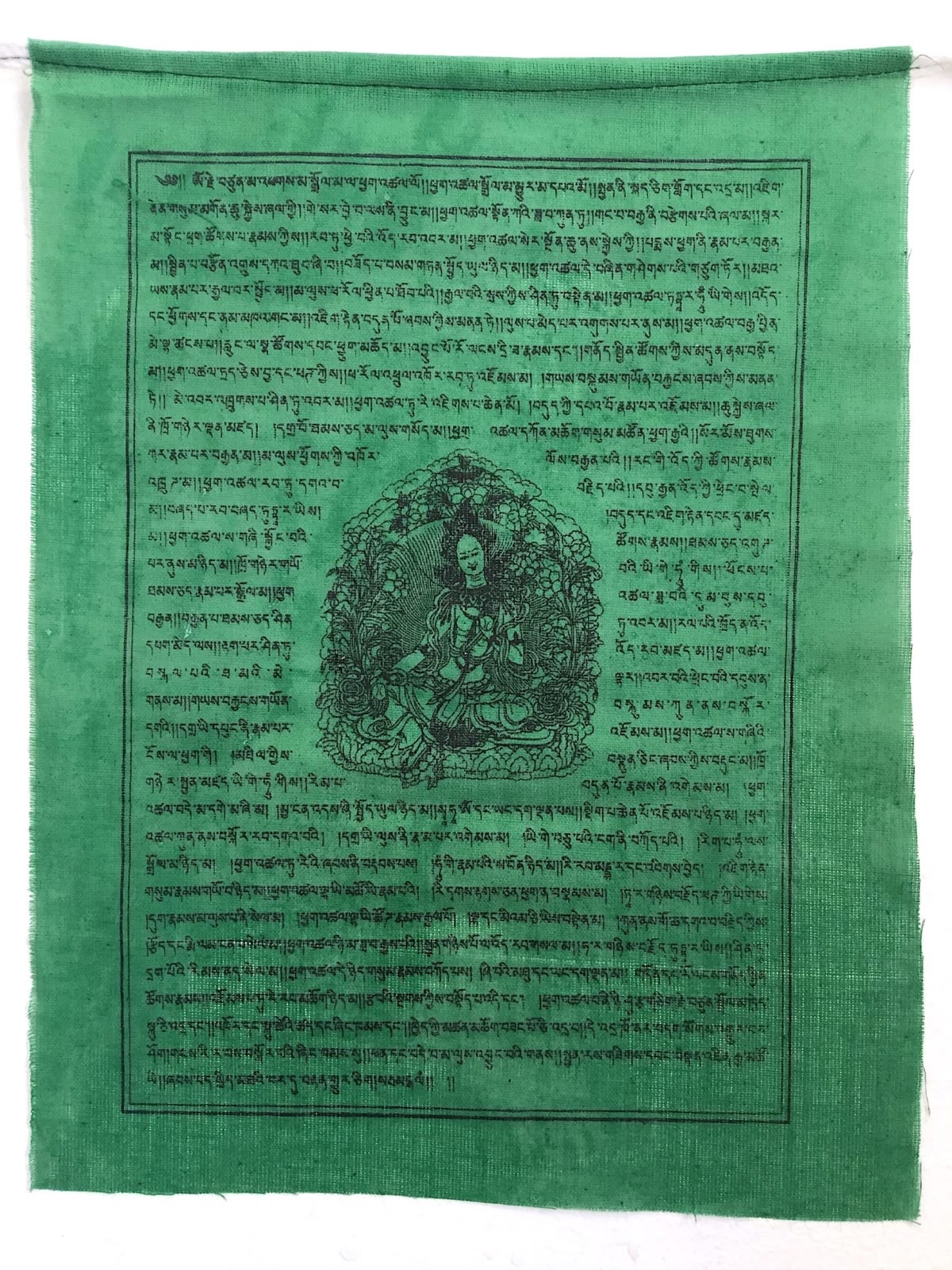 A green prayer flag printed with a deity figure and fine lines of Tibetan script