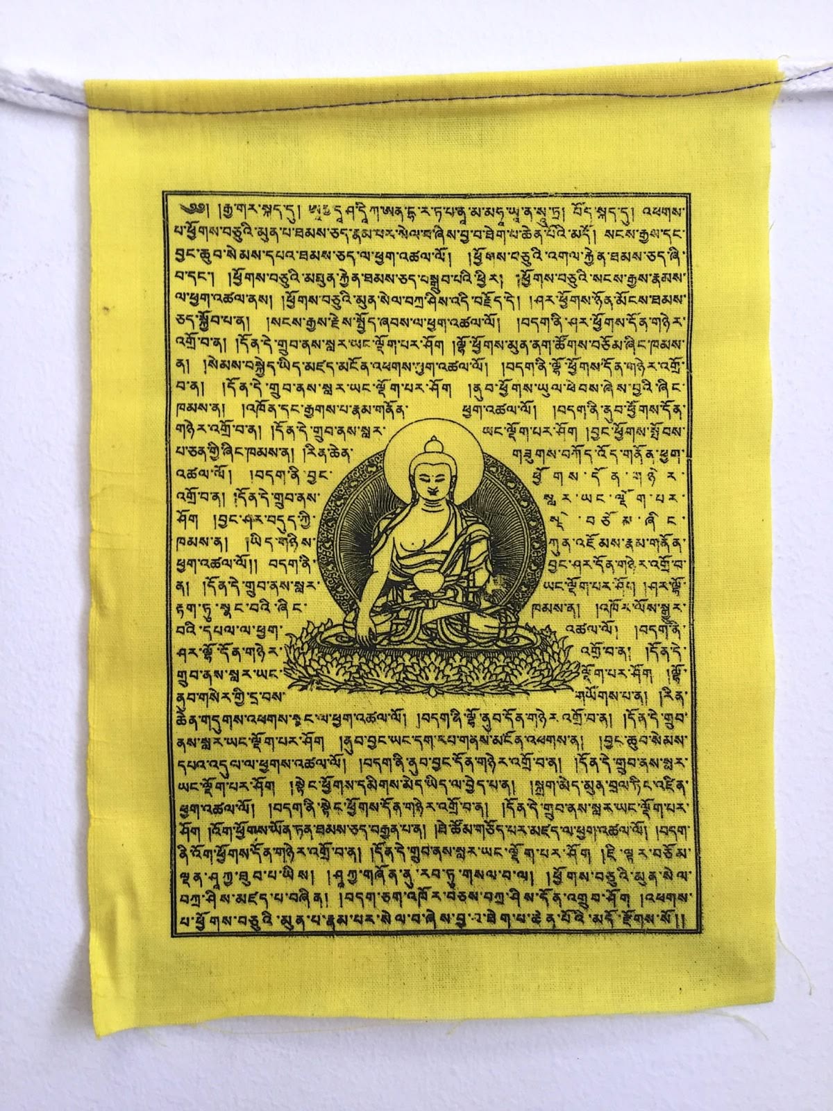 A yellow prayer flag printed with a seated Buddha and Tibetan mantras