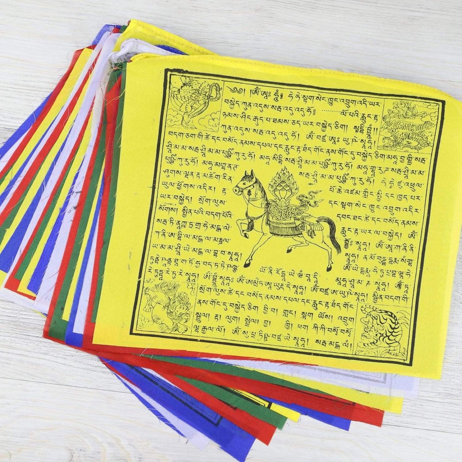 A stack of five-colour prayer flags with a yellow flag showing the wind horse on top