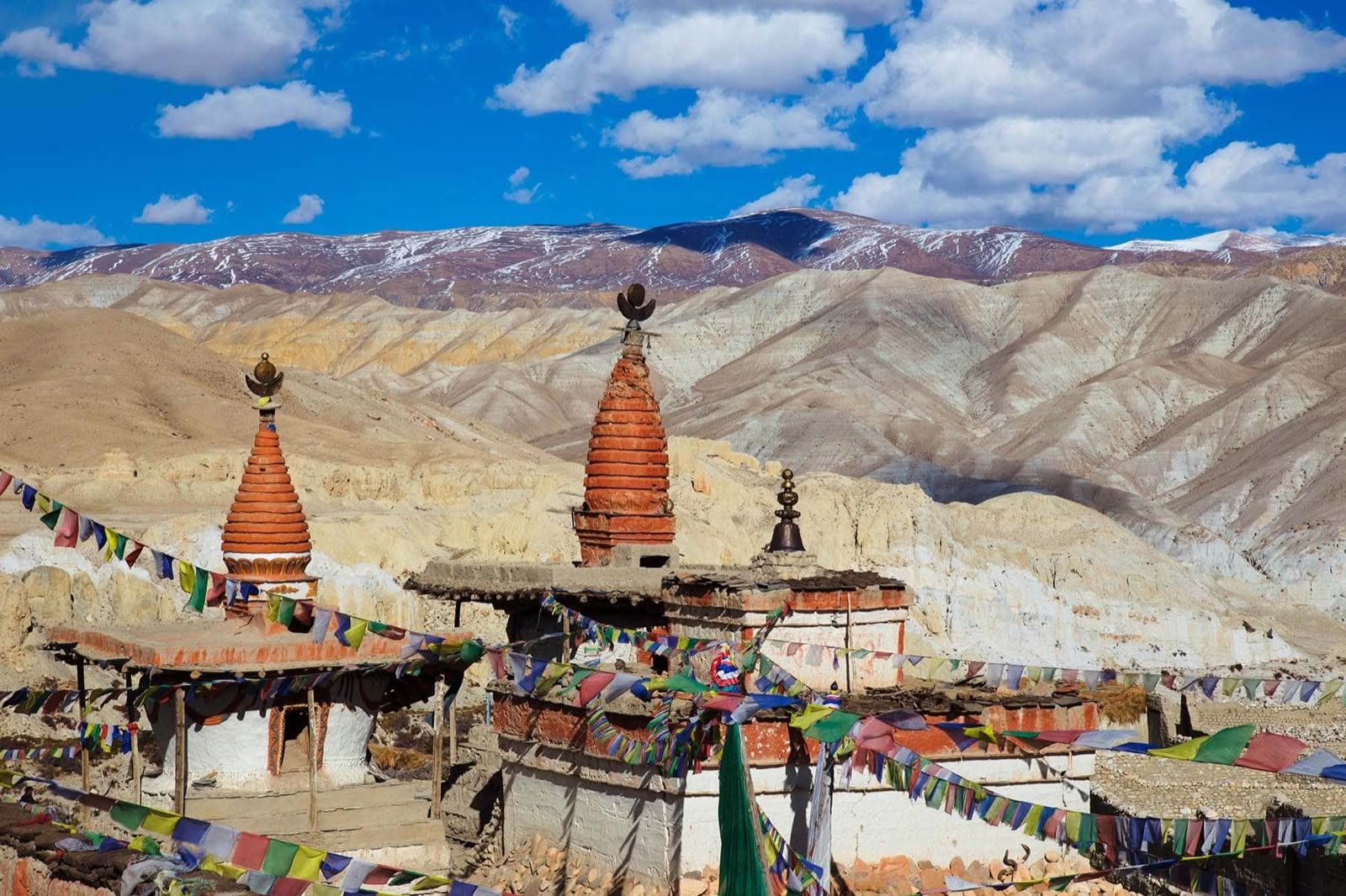 Stupas and prayer flags on a dry, barren Himalayan mountainside under a blue sky