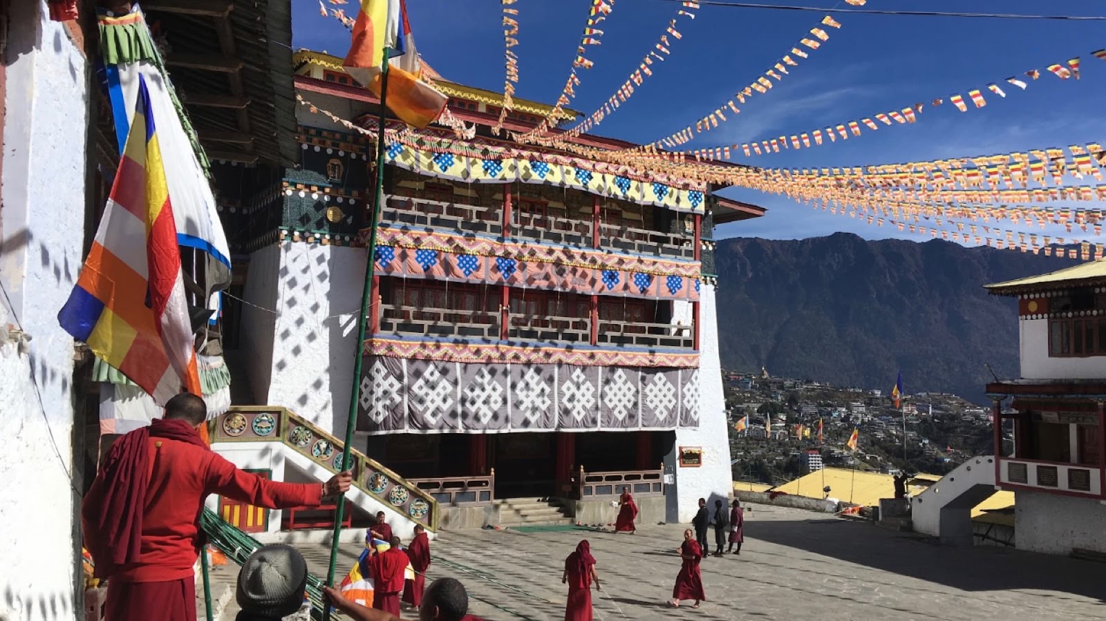 Tawang Monastery courtyard with monks in maroon robes under lines of prayer flags