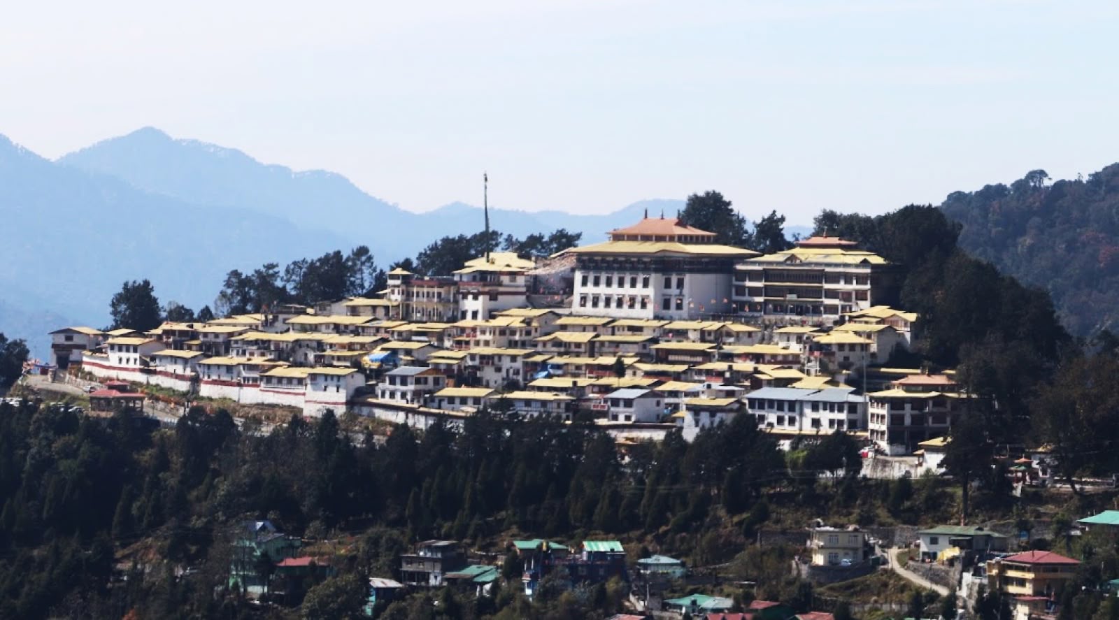Tawang Monastery seen from a distance on a forested ridge with mountains behind