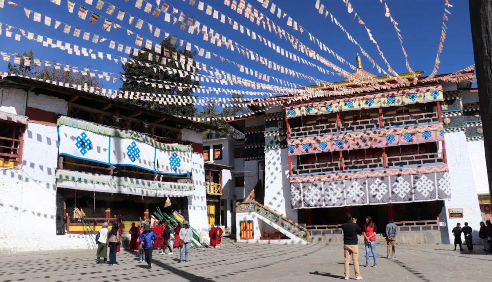 Visitors and monks in the courtyard of Tawang Monastery under strings of prayer flags