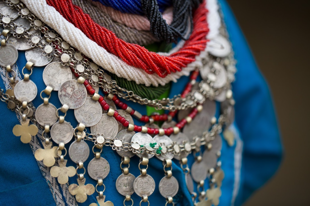 Close-up of layered red, white and blue bead strands with silver coin necklaces and coin pendants on a blue garment