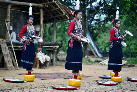 Three young Reang women in traditional dress performing the Hojagiri dance, each balancing a pot with a lamp on her head while standing on a small yellow pot
