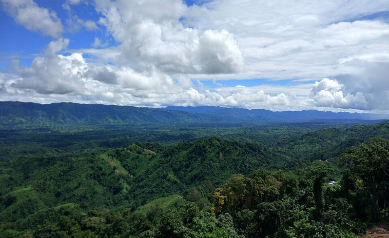 View over forested green hills and distant ridges under a cloudy blue sky in Tripura